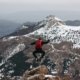 jumping man on rock facing mountains with snow