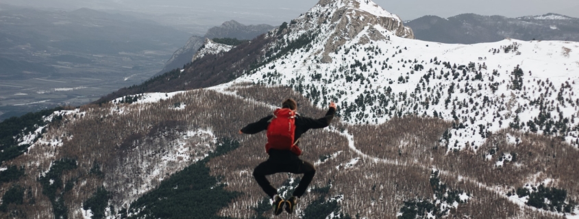 jumping man on rock facing mountains with snow